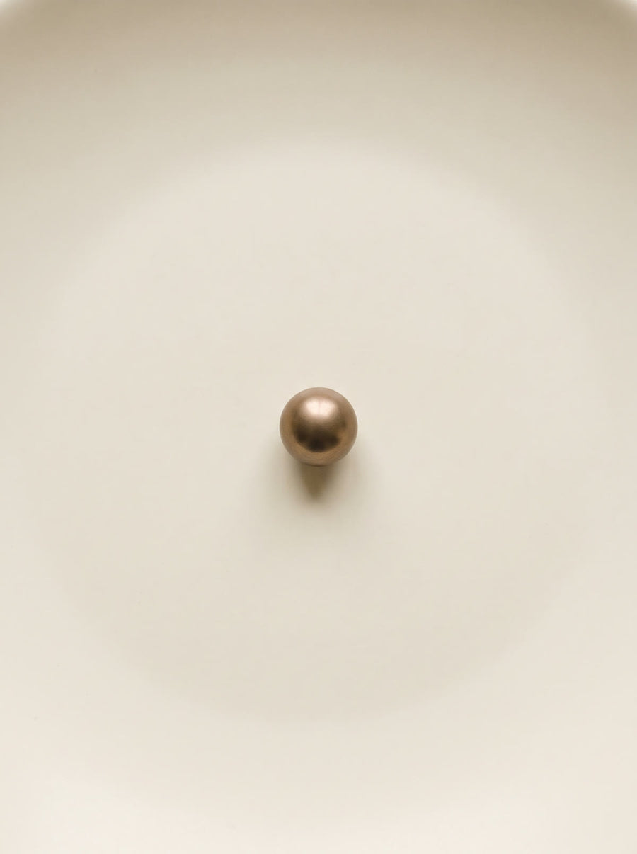 A single bronze sphere come to rest on a smooth ivory surface
