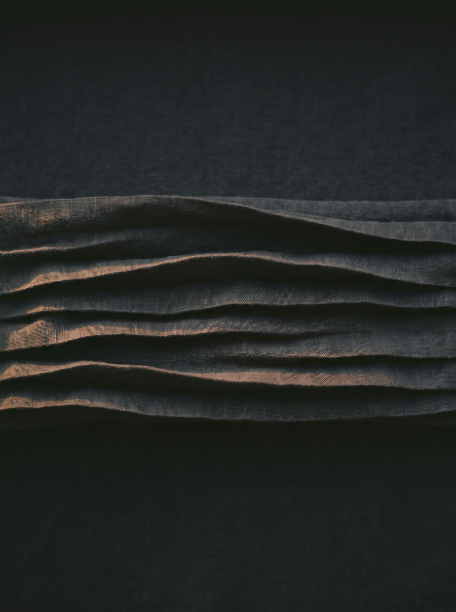 Dark charcoal linen pleated into a slow wave in low evening light
