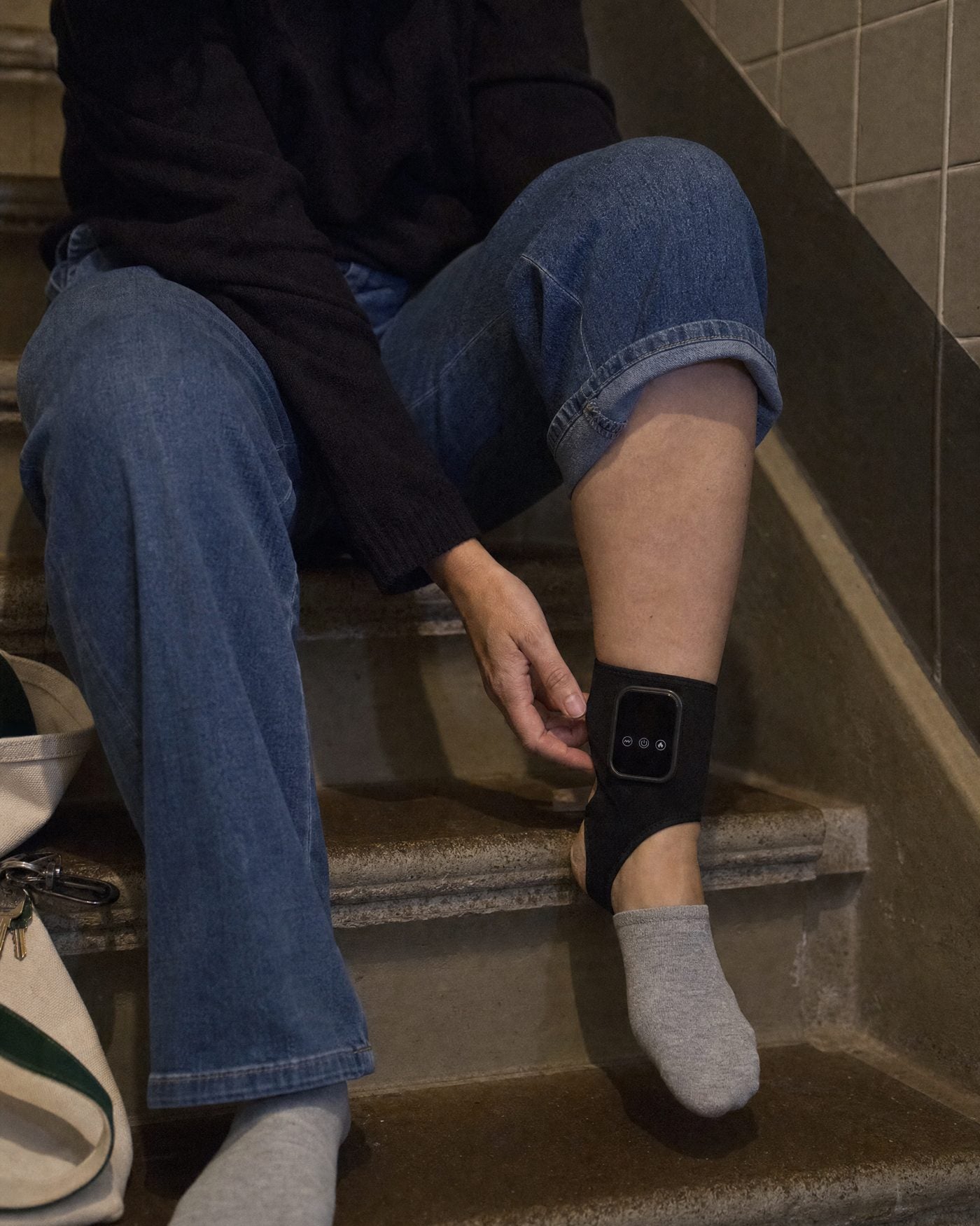 Sitting on the bottom steps of a stairwell at night, bag set down, wrap on one ankle