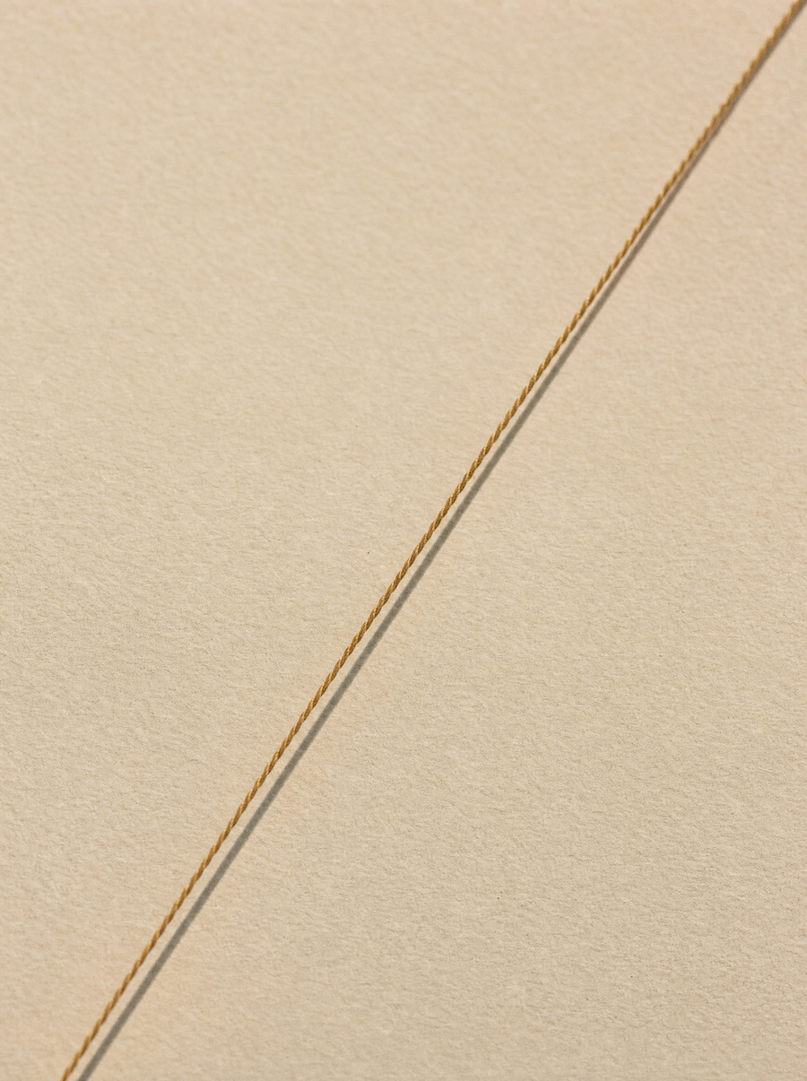 A single taut bronze thread across cream paper